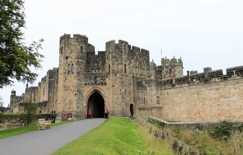 The stone gatehouse and battlemented walls of Alnwick Castle, with a path leading up to its arched entrance