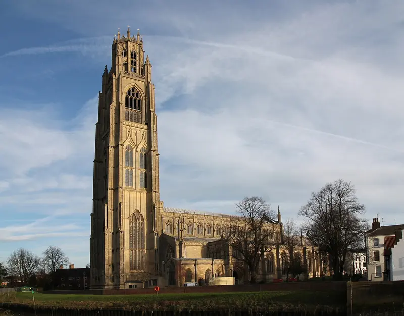 The tall lantern tower of St Botolph's Church, 'The Stump', and its long nave glowing in low winter sun, seen across a green with bare trees