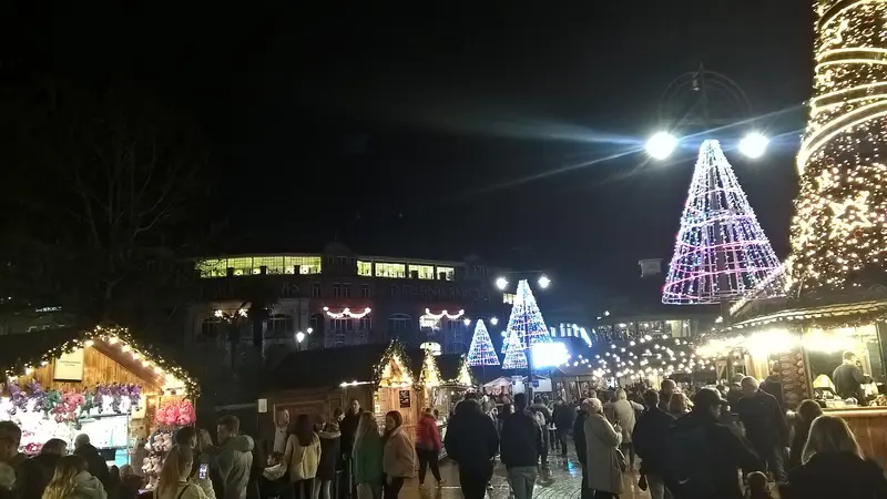 Crowds walking between lit wooden market chalets at night in Bournemouth, beneath cone-shaped Christmas light trees and a light-wrapped tower
