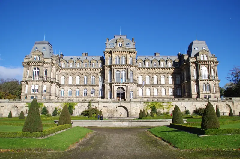 The grand French-château-style front of the Bowes Museum, with clipped yew trees on the lawns before it under a blue sky