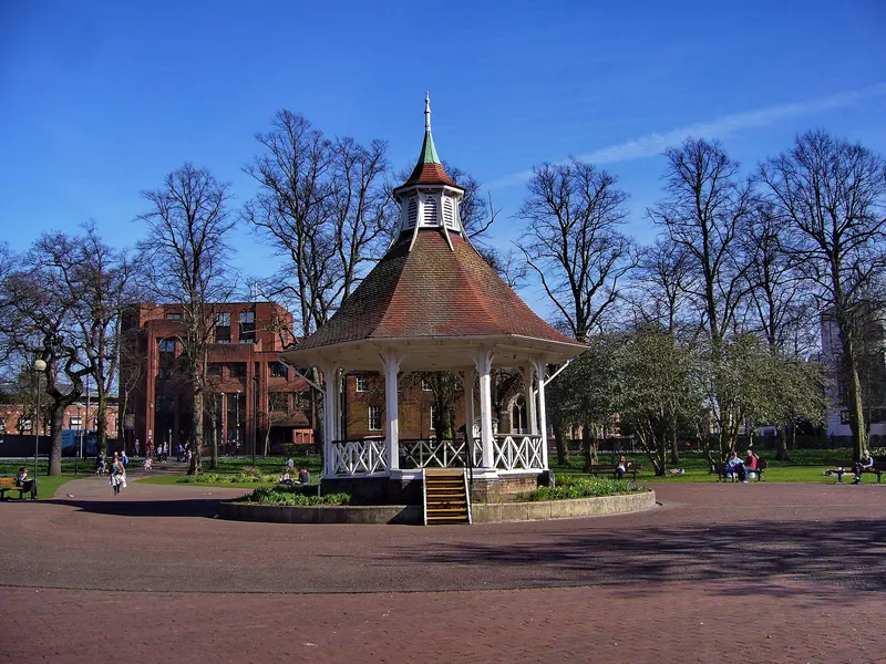 The white-pillared bandstand with a red-tiled roof in Chapelfield Gardens, among bare trees under a deep blue sky