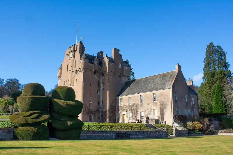 The pink-harled tower house of Crathes Castle with its turrets, beside clipped yew hedges and a lawn under a clear blue sky