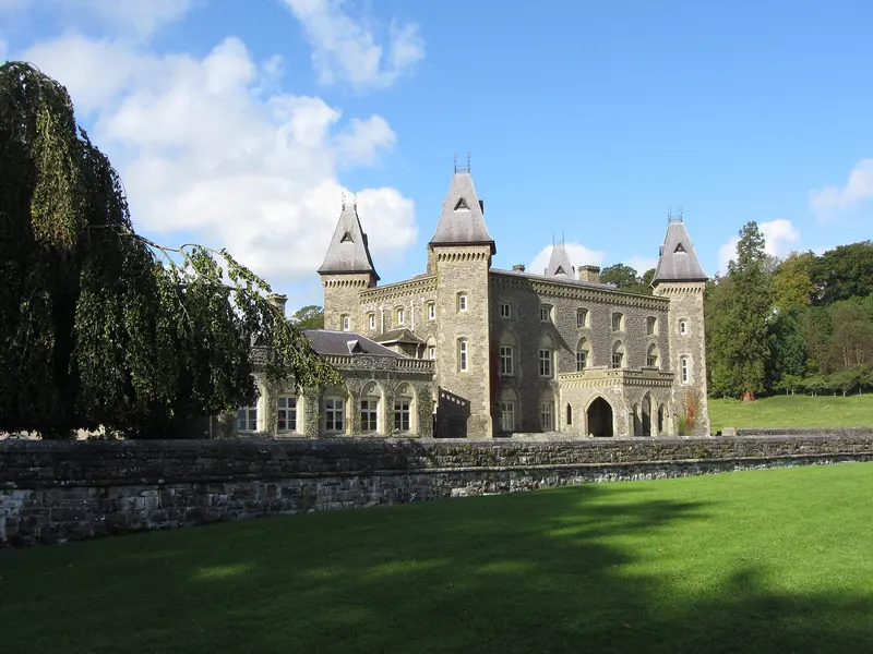 The grey stone Newton House at Dinefwr, with pointed corner turrets, behind a sloping lawn and stone wall