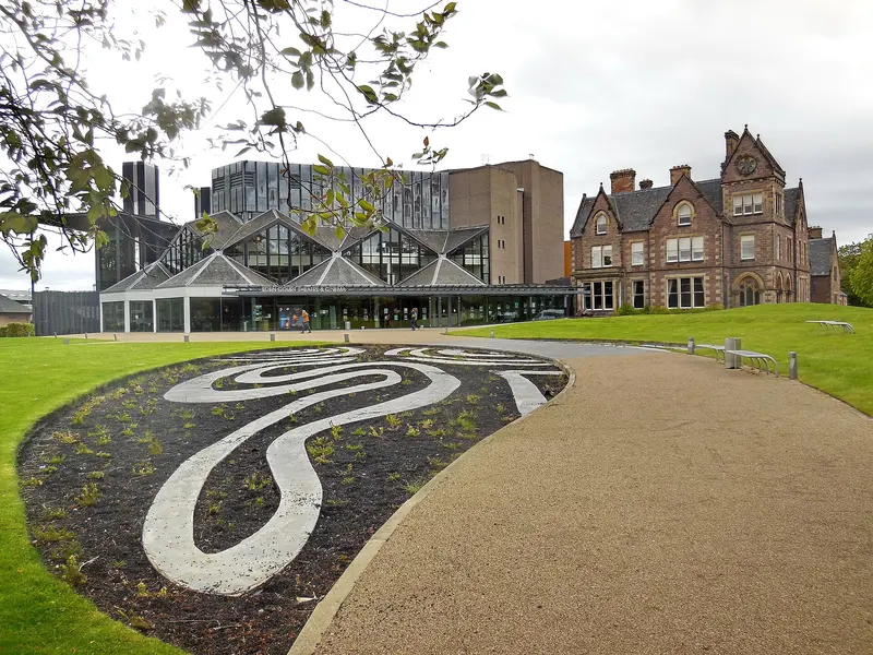 Eden Court's modern glass-fronted theatre beside the Victorian stone Bishop's Palace, with a curving path and a decorative pebble lawn in front