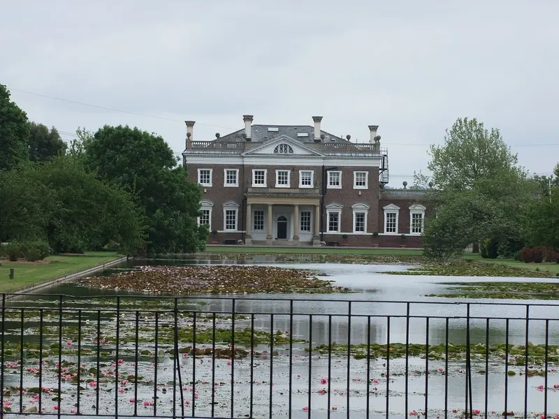 The Georgian brick front of Boreham House, with a pedimented centre, beyond a long lily pond behind railings