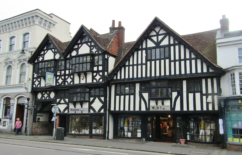 A row of black-and-white timber-framed buildings with steep gables on The Borough in Farnham, beside a Georgian stuccoed building