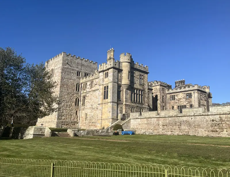 The battlemented stone towers and walls of Ford Castle across a sunlit lawn under a blue sky