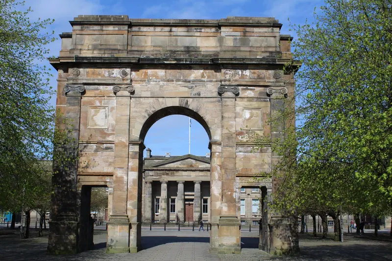 The weathered sandstone McLennan Arch framed by spring trees, with a columned court building seen through the arch