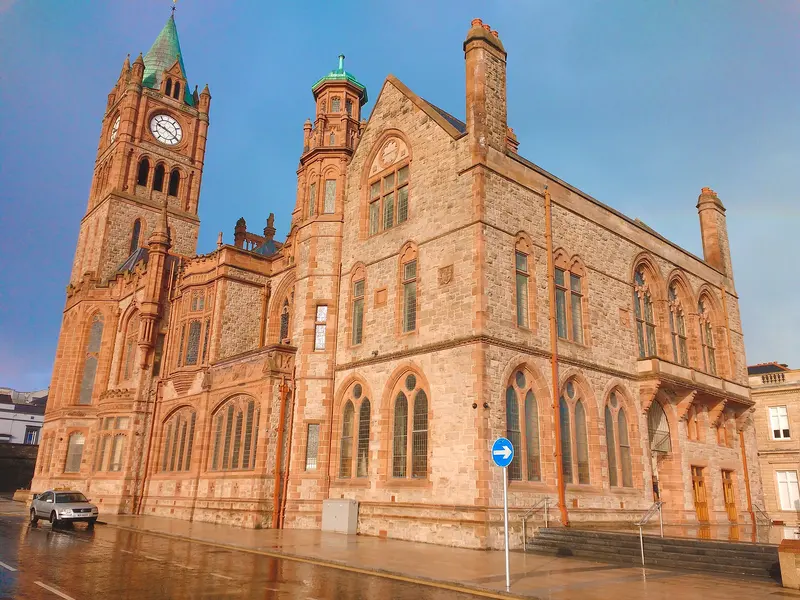 The ornate red sandstone Guildhall in Derry, with its clock tower and tall Gothic windows, glowing in low sunlight
