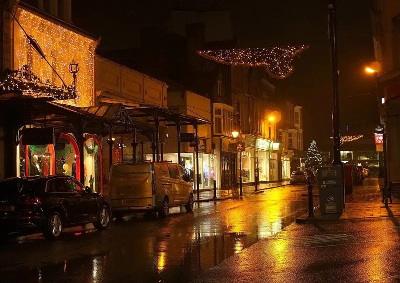 James Street in Harrogate on a wet night, with a shopfront draped in fairy lights, glass canopies, a lit Christmas tree and light garlands across the street