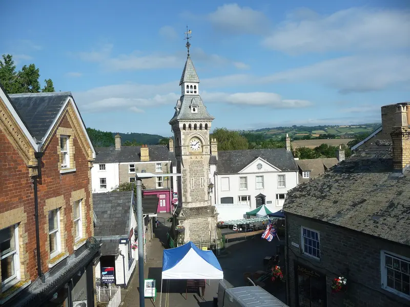 Hay-on-Wye's Victorian stone clock tower rising above slate roofs and a small street market with gazebo stalls, with green hills beyond