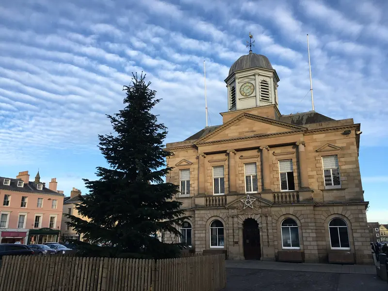 A tall Christmas tree beside Kelso's sandstone Town House, with its clock cupola, in the town square under a rippled blue sky
