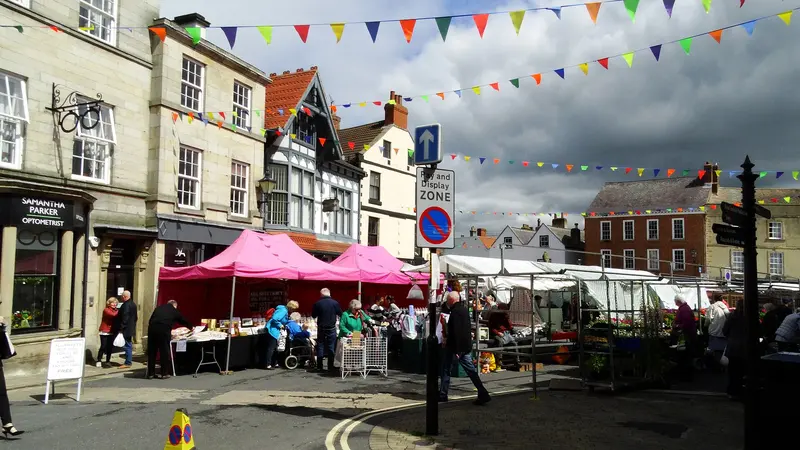 Market stalls with pink and white canopies in Knaresborough Market Place under strings of colourful bunting, with old shopfronts around the square