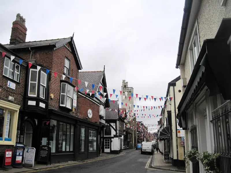 Knutsford's narrow King Street lined with brick and timber-framed shops under strings of bunting, with a tall stone tower at the far end