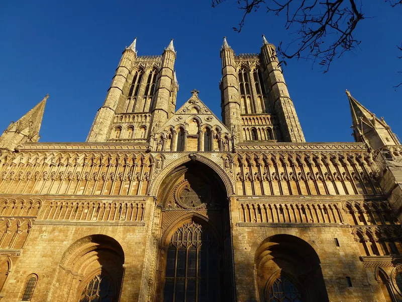 The richly carved west front and twin towers of Lincoln Cathedral glowing gold in winter sunlight against a deep blue sky