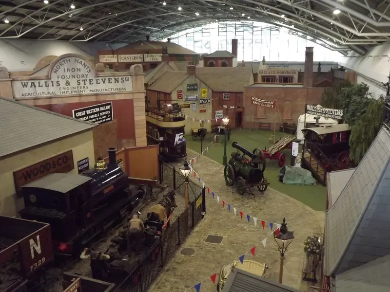 The indoor recreated Victorian street at Milestones Museum under its arched glass roof, with old shopfronts, a steam engine and a cobbled road hung with bunting