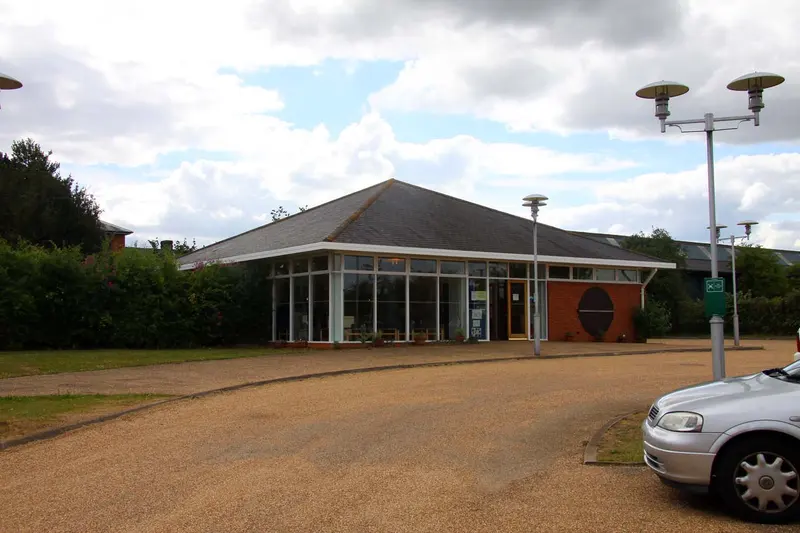 The low glass-fronted entrance building and shop of Milton Keynes Museum beside a gravel forecourt and lamp posts