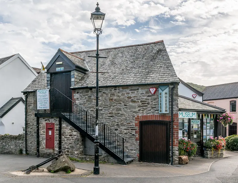 The old stone Bakehouse Centre in Braunton, with an outside staircase, a red postbox and a Victorian lamp post, under a bright cloudy sky