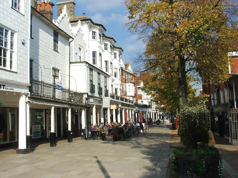 The Pantiles in Royal Tunbridge Wells, a paved Georgian walk with a white colonnade of shops and cafe tables beneath autumn trees