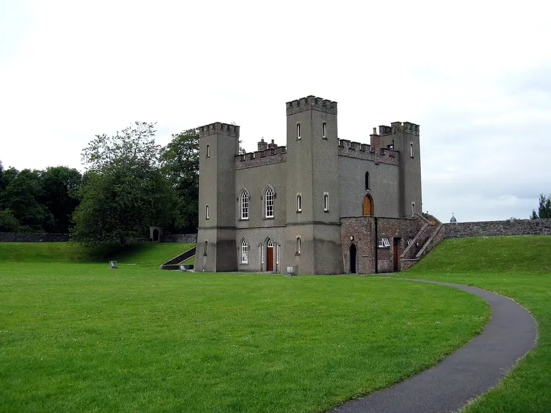 The grey battlemented gatehouse of Hillsborough Fort with its corner turrets, standing on a wide lawn with a curving path