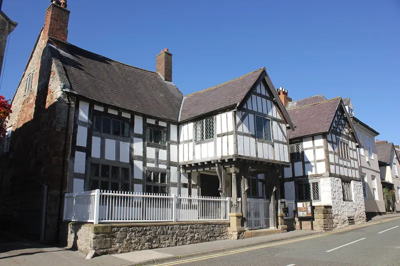 The black-and-white timber-framed front of Nantclwyd y Dre in Ruthin, with a white picket fence, on a quiet street under a clear blue sky