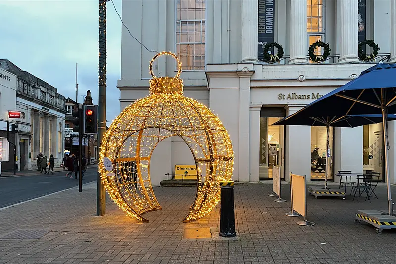 A giant walk-through bauble made of golden lights outside the white columned St Albans Museum, whose windows are hung with Christmas wreaths