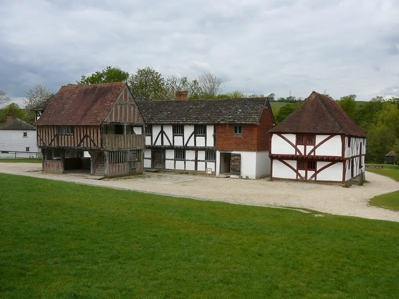 A row of rescued timber-framed medieval buildings with steep tiled roofs beside a gravel path and lawn at the Weald & Downland Living Museum